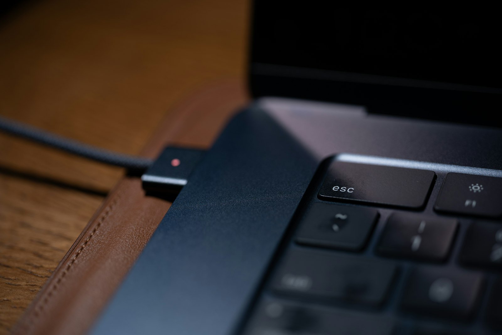 Close-up of a laptop edge and connected cable on a wooden desk