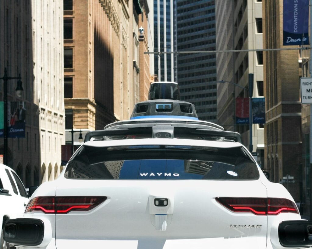 Rear of a white Waymo-branded Jaguar vehicle with roof-mounted sensors on a city street; illustrative photo, not Singapore
