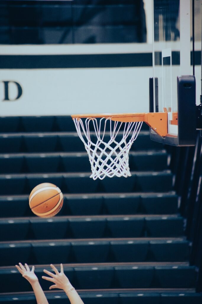 Two basketball players reaching for the ball beneath a hoop during a game