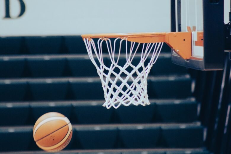 Two basketball players reaching for the ball beneath a hoop during a game