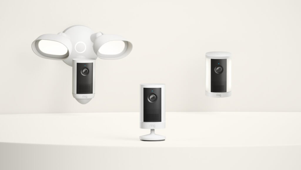 Three white Ring security cameras: a dual-floodlight camera, a tabletop camera, and a spotlight camera