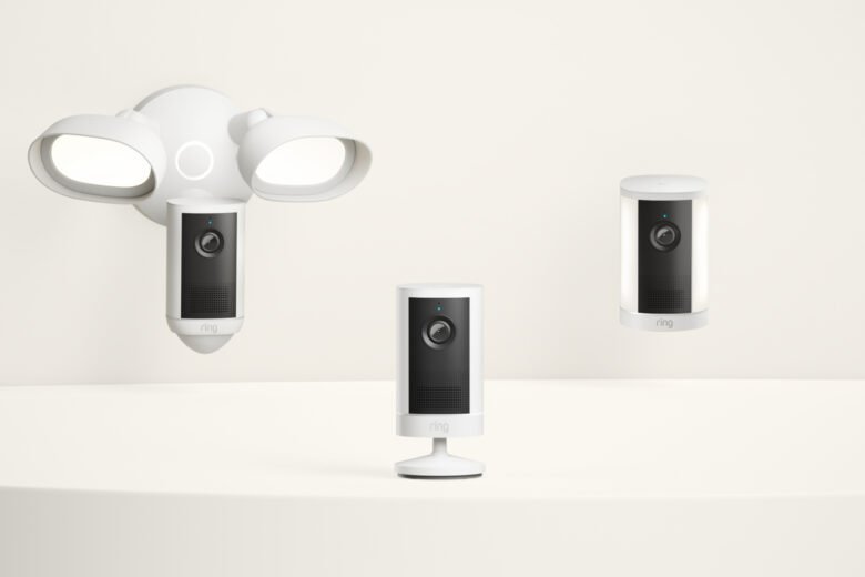 Three white Ring security cameras: a dual-floodlight camera, a tabletop camera, and a spotlight camera